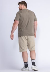Šedé bavlněné tričko, béžové šortky s kapsami a šedé tenisky s bílými akcenty. Model se otáčí zády, ukazuje uvolněný střih a design.