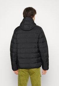 Black puffer jacket with a quilted pattern and attached hood, featuring a smooth, shiny texture. Worn with green corduroy pants.