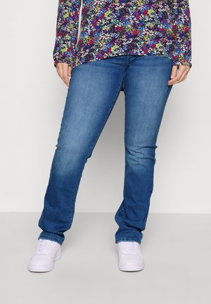 Jeans blu in design a gamba dritta, caratterizzati da una texture denim liscia. Indossati con sneaker bianche, abbinati a una blusa a maniche lunghe con motivo floreale.