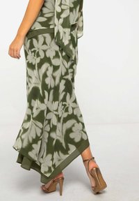 Falda de estampado floral verde con un diseño fluido y suave al tacto, terminada con un dobladillo sólido de color verde oscuro. Combinada con tacones marrones de tiras.