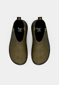 Chaussures slip-on vert olive en suède avec une finition texturée, semelle en caoutchouc noir, surpiqûres jaunes et une languette noire au talon.