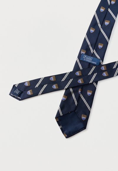 Γραβάτα από μπλε ναυτικό μετάξι με λευκές διαγώνιες ρίγες και μικρά μπλε και χρυσά εμβλήματα σε σχήμα ασπίδας, με ετικέτα Polo by Ralph Lauren, κατασκευασμένη στην Ιταλία.
