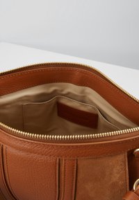 Indvendig i en brun læderhåndtaske med en glat beige foer og en lille lomme. Har en guldfarvet lynlås og subtile teksturvariationer.