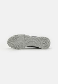 Suela de zapato deportivo negro con una suela de goma texturizada gris, que presenta indentaciones ovaladas para mayor agarre y un logo sutil cerca del talón.