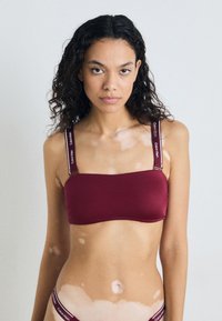 Bordo bralet s trakama s otisnutim logotipom. Glatka tkanina, pravokutni oblik, minimalistički dizajn, bešavne rubove.