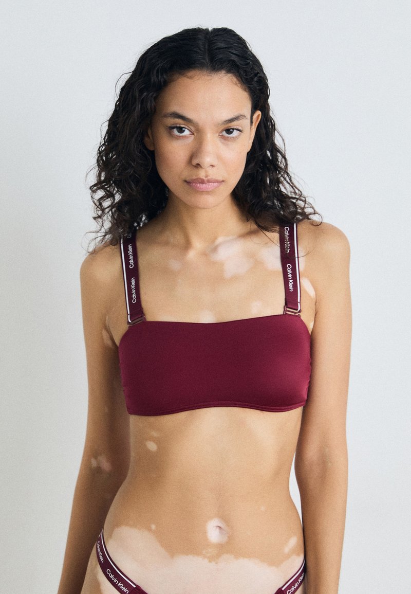 Bordo bralet s trakama s otisnutim logotipom. Glatka tkanina, pravokutni oblik, minimalistički dizajn, bešavne rubove.