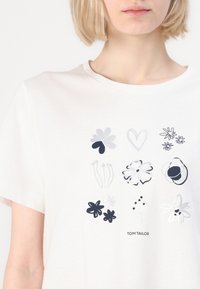 T-shirt en coton blanc avec une impression florale variée à l'avant en bleu marine et argent. Encolure ronde, manches courtes, coupe décontractée.