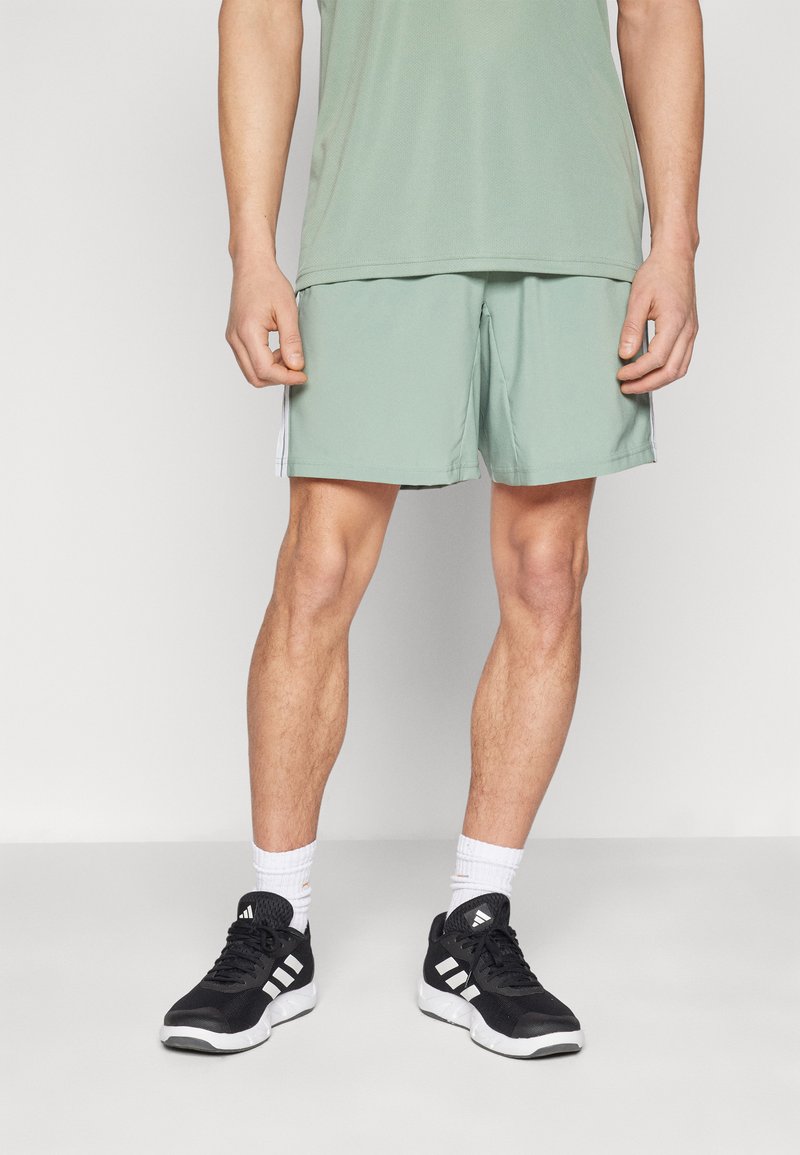 Mintgrüne Sportshorts mit seitlichen Streifen, getragen mit schwarzen Sneakers und weißen Socken. Das Oberteil ist ein passendes mintgrünes Shirt.