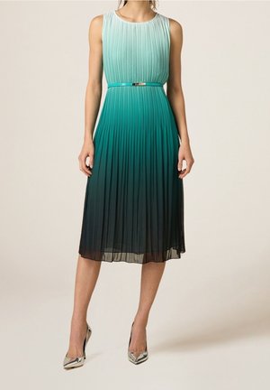Ærmeløs plisseret midi-kjole med grøn til sort ombré-gradient, tyndt metalbælte, båret med sølvfarvede spidse høje hæle.