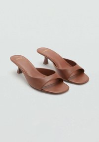 Brown leather slip-on mules with open toe, wide crossing straps, and a short, flared heel. Smooth texture and minimalistic design.