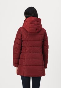 Doudoune rouge avec capuche, dotée d'un design matelassé horizontal et d'un col arrondi. Fabriquée dans un matériau lisse et léger.