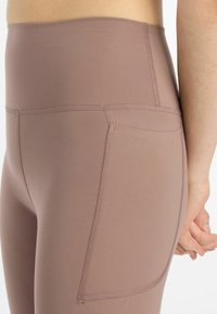 Hohe, mauvefarbene Leggings aus Stretchstoff mit glatter Textur, ausgestattet mit einer Seitentasche und Flachnähten.