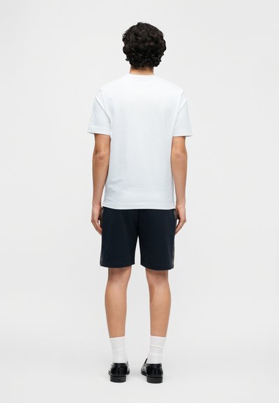 Ανοιχτό μπλε βαμβακερό t-shirt με κοντά μανίκια, άνετη εφαρμογή, συνοδευόμενο από σκούρο σορτς, λευκές κάλτσες και μαύρα παπούτσια; απεικονίζεται από πίσω.