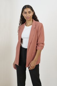 Saka z jemné růžové látky, jednobarevný design s ohrnutými rukávy, spárované s bílým žebrovaným topem a černými kalhotami. Minimalistické kapsy.