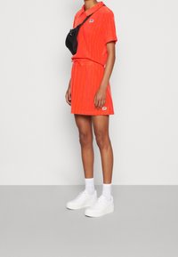 Rood gestreepte polo jurk gemaakt van zachte stof, met een aansluitende taille en korte mouwen. Gecombineerd met chunky witte sneakers en een zwarte crossbody tas.