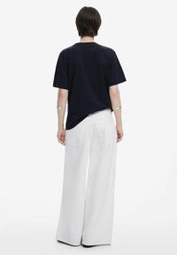 Navy Baumwoll-T-Shirt mit kurzen Ärmeln, entspannte Passform. Kombiniert mit weiten, weißen Jeanshosen mit hinteren Taschen und einer glatten Textur.