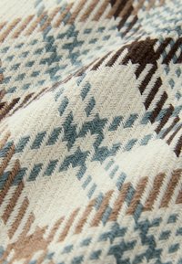 Gros plan d'un tissu tissé avec un motif en zigzag dans des couleurs beige, bleu clair, marron et crème, montrant une texture détaillée.