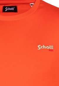 T-shirt in cotone arancione con scollo rotondo e un sottile logo ricamato "Schott NYC" in oro e viola sul davanti.