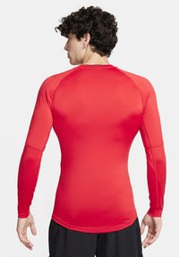 Rød langærmet træningsshirt lavet af strækbart materiale, med en tætsiddende design og raglanærmer for bedre bevægelsesfrihed.