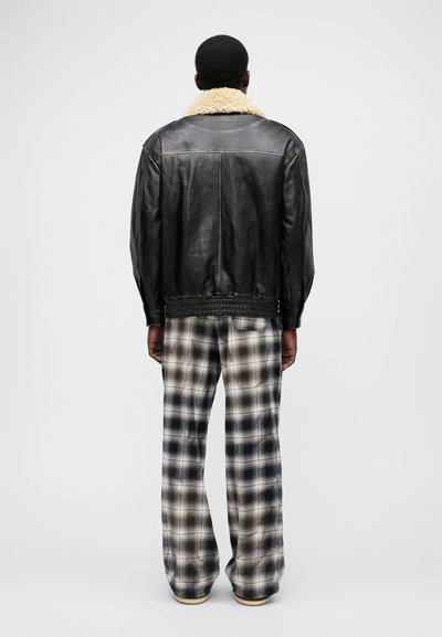 Veste en cuir noir avec un col en fausse fourrure crème, associée à un pantalon écossais large dans des tons beiges, bleus et noirs.