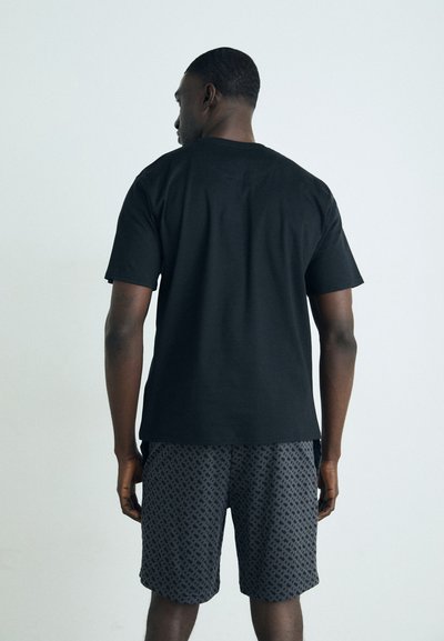T-shirt en coton noir à manches courtes, associé à un short gris à motifs présentant un design géométrique, vu de dos.