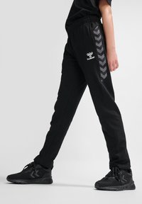 Schwarze Sporthose mit einem strukturierten Seitenpaneel mit einem Chevron-Muster und einem elastischen Bund. Logo auf der linken Vorderseite.