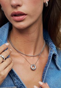 Silversmycken i kedjor som är lager på lager runt halsen, med en cirkulär medaljong med en glänsande yta och en liten klar detalj.