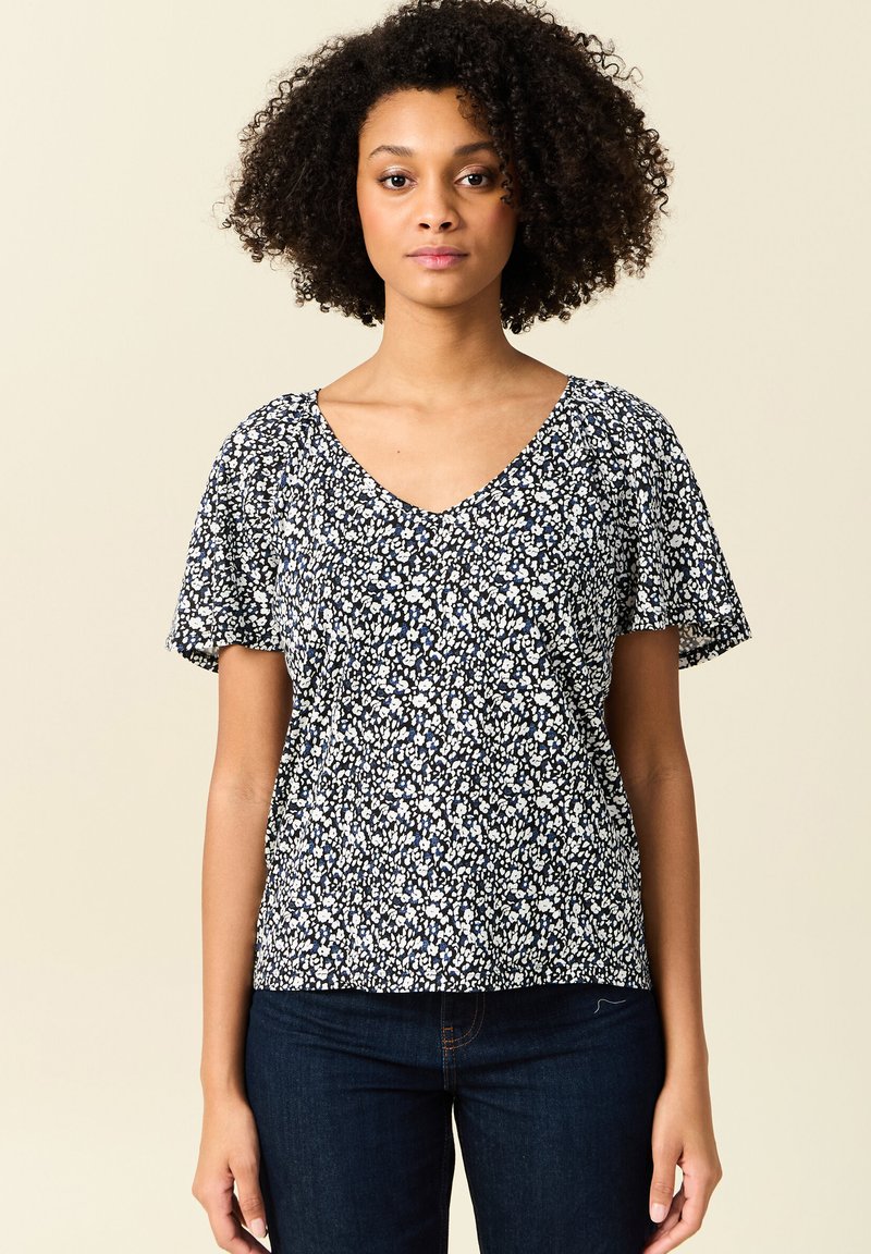 Top floreale a V in navy con motivi bianchi e azzurri. Maniche corte, tessuto morbido, vestibilità comoda, abbinato a jeans in denim scuro.
