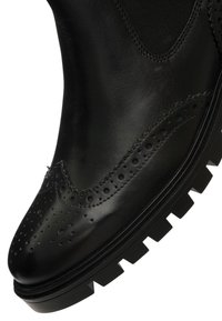 Czarny skórzany but brogue z perforowanymi detalami i solidną podeszwą, zbliżenie na czubek i bok.