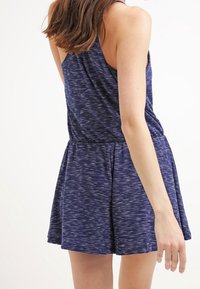 Robe sans manches bleu marine avec un motif texturé, taille cintrée et jupe évasée. Le tissu semble doux et léger.