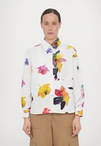 Floral button-up shirt with a white background, featuring colorful flower patterns in pink, yellow, orange, and purple; includes a chest pocket.