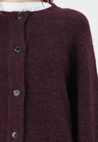 Burgundy knit cardigan with a textured finish, featuring a round neckline and five prominent black buttons down the front.