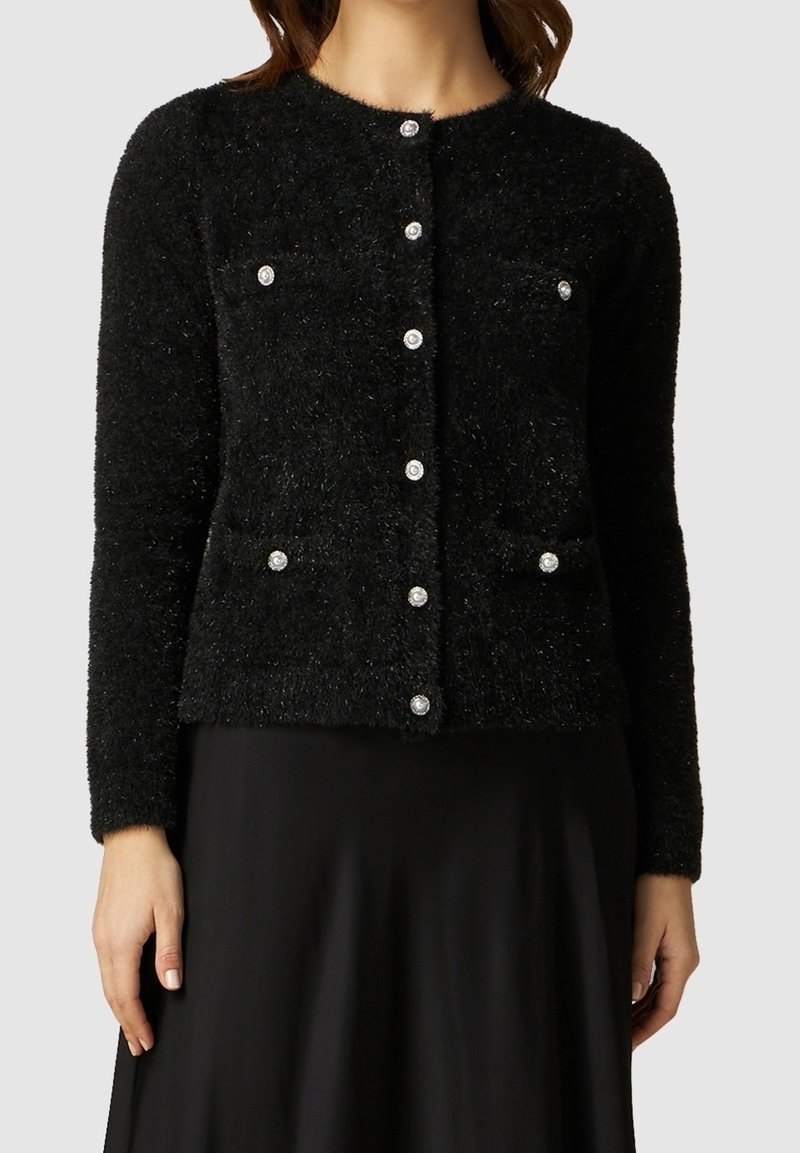 Svart fluffig cardigan med långa ärmar, rund hals och sex knäppningar med rhinestones. Två bröstfickor synliga.