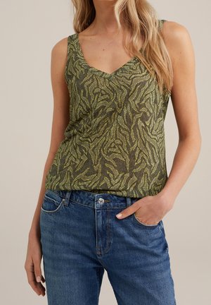 Vihreä hihaton paita, jossa on V-pääntie, ja jolla on tumman vihreä ja keltainen teksturoitu lehtikuvio. Yhdistetty sinisiin farkkuihin.