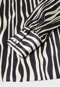 Poignet de chemise à manches longues à rayures verticales noires et blanches avec deux boutons recouverts de tissu sur un tissu lisse.