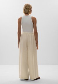 White tank top paired with flowy, cream-colored, vertically striped wide-leg pants. The fabric is lightweight with an elastic waistband.