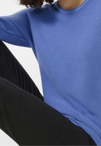 Suéter de punto ribeteado azul con un escote redondeado, que presenta rayas texturizadas, combinado con pantalones negros ajustados.