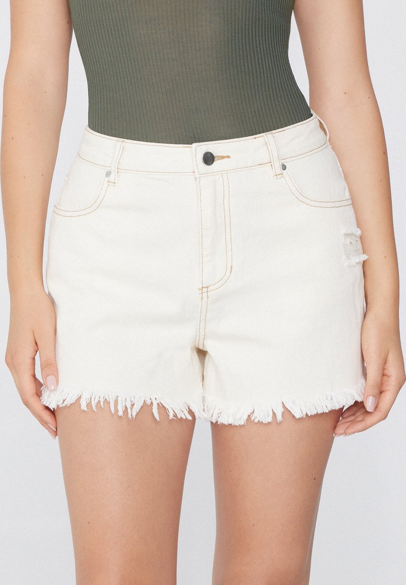 Shorts en denim blanc avec ourlet effiloché, design à cinq poches et une seule pièce déchirée. Fermeture à bouton et détails de couture subtils.