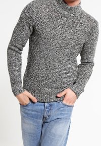 Grijze en zwarte gemarmerde gebreide turtleneck trui met lange mouwen en ribgebreide manchetten, gecombineerd met blauwe denim jeans. De textuur lijkt zacht te zijn.