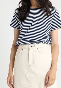Námořnický a bílý pruhovaný bavlněný tričko s krátkými rukávy, kulatým výstřihem a kapsičkou na hrudi, spárované s džínovou sukní světlé barvy.