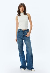 Top sin mangas de canalé blanco combinado con jeans de pierna ancha de cintura alta en azul, que cuentan con un diseño clásico de cinco bolsillos y cierre de botón.