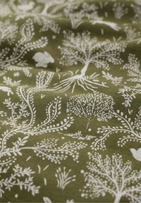 Olijfgroene stof met witte botanische patronen van bomen, bladeren en kleine dieren, wat een natuurlijk thema en een textuurachtige uitstraling geeft.