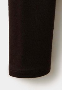 Gros plan sur le poignet d'une longue manche noire en tricot avec des coutures visibles le long de l'ourlet sur un fond clair.