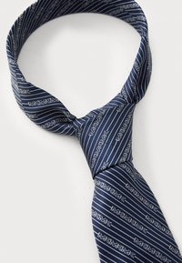 Cravate en soie marine avec des rayures blanches diagonales et un motif de logo répété. Le tissu a une texture lisse avec une finition brillante.