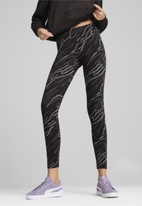 Zwarte en grijze tigergestrekte leggings met een hoge tailleband, gemaakt van gladde stof. Gecombineerd met lichtpaarse sneakers.