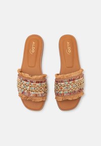 Brune glidesandaler med dekorative vevde stropper som har flerfargede perler og frynseaccents. Myk fotramme for komfort.