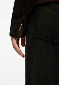 Hand met zilveren ring die tevoorschijn komt uit een zwart top met lange mouwen en textuur, naast een zwart kledingstuk met een zichtbare achterzak.