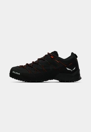 Zwarte lage wandelschoenen met oranje-accentluik, een gestructureerde gripzool en reflecterende logo's aan de neus en achterkant.