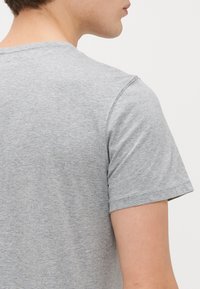 Pilkos spalvos medvilnės marškinėliai su apvaliu iškirpimu ir trumpomis rankovėmis. Audinys turi lygų paviršių su nedideliu heather raštu.