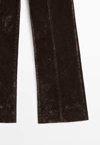 Pantaloni in corduroy marroni con gambe larghe, una texture morbida e evidenti righe verticali. Nessuna hardware o accentuatura visibile.